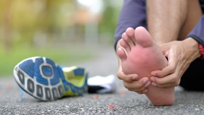 Close-up of a person holding their foot, indicating pain, with a running shoe nearby.
