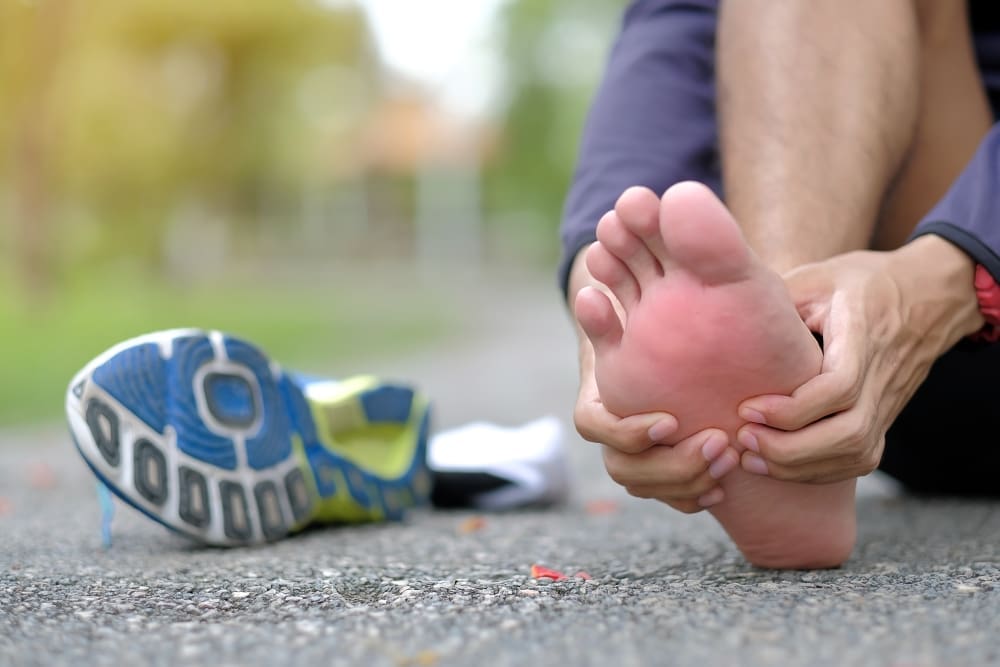 Close-up of a person holding their foot, indicating pain, with a running shoe nearby.