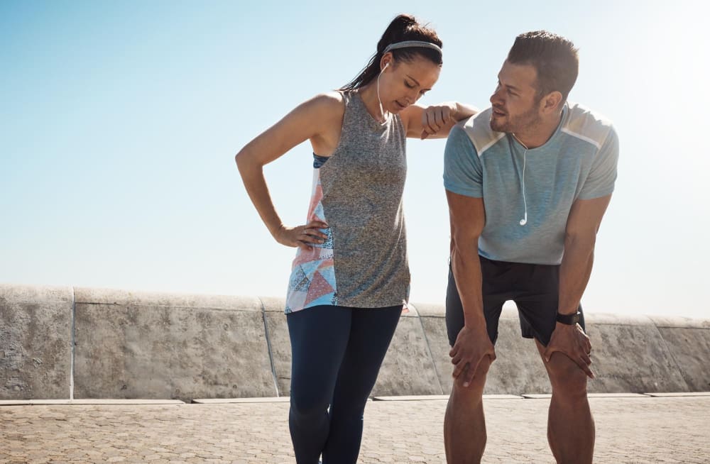 Two exhausted runners taking a break, one leaning on the other, suggesting fatigue or a potential injury.