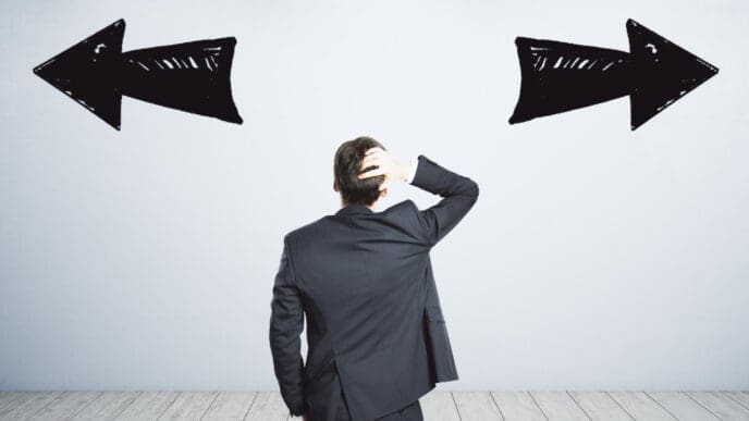 A man in a dark suit stands with his back to the viewer, scratching his head, facing a white wall with two large, hand-drawn black arrows pointing in opposite directions, symbolizing confusion or conflicting choices.