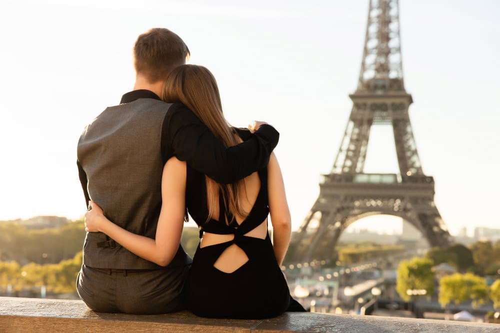 A couple embracing while sitting and looking at the Eiffel Tower in Paris, bathed in golden sunlight.