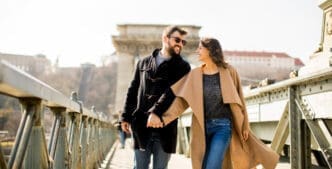 A happy couple holding hands and smiling at each other while walking on the Széchenyi Chain Bridge in Budapest.