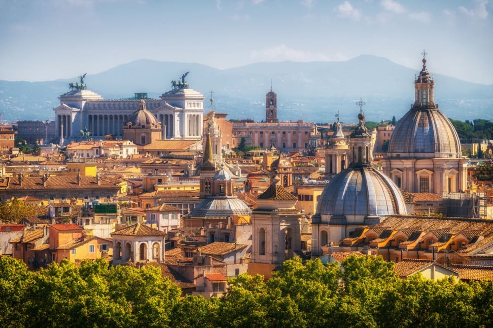 Panoramic view of Rome's skyline with numerous domes and historic buildings, including the Altar of the Fatherland, and distant mountains.