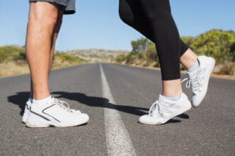 Close-up of two pairs of feet in running shoes, standing on a road with a white line, facing each other.