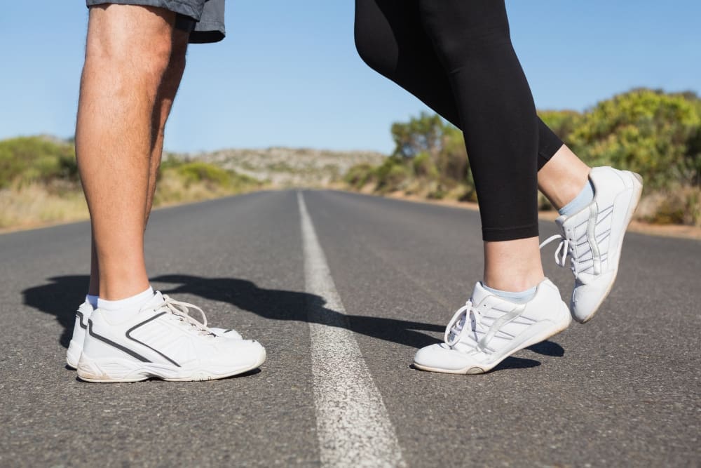 Close-up of two pairs of feet in running shoes, standing on a road with a white line, facing each other.