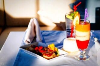 A beautifully presented meal with two drinks on a table, including a layered red, white, and orange cocktail and a plate with seared scallops garnished with edible flowers.
