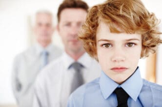 A serious young boy with curly blonde hair wears a blue shirt and black tie, looking directly at the camera, with two blurred adult men in business attire standing behind him, symbolizing lineage or succession.
