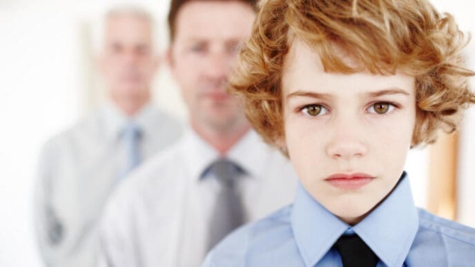 A serious young boy with curly blonde hair wears a blue shirt and black tie, looking directly at the camera, with two blurred adult men in business attire standing behind him, symbolizing lineage or succession.