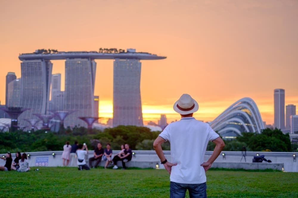 A person in a hat viewing the Marina Bay Sands complex and Gardens by the Bay in Singapore at sunset.