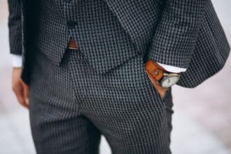 Close-up of a man in a patterned grey suit with a watch on his wrist, hand in pocket.