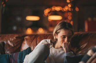 A candid portrait of a teenager sitting on a leather couch in a dimly lit, cozy room with blurred lights in the background, appearing contemplative or somber.
