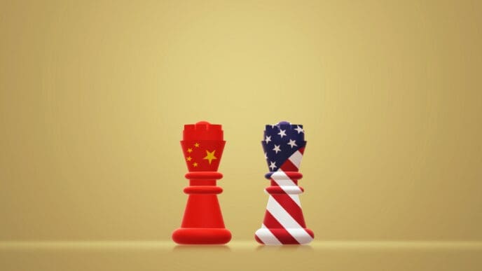 Two stylized chess rooks, one red with a Chinese flag design and the other striped with an American flag design, stand facing each other on a golden surface, symbolizing a geopolitical standoff.