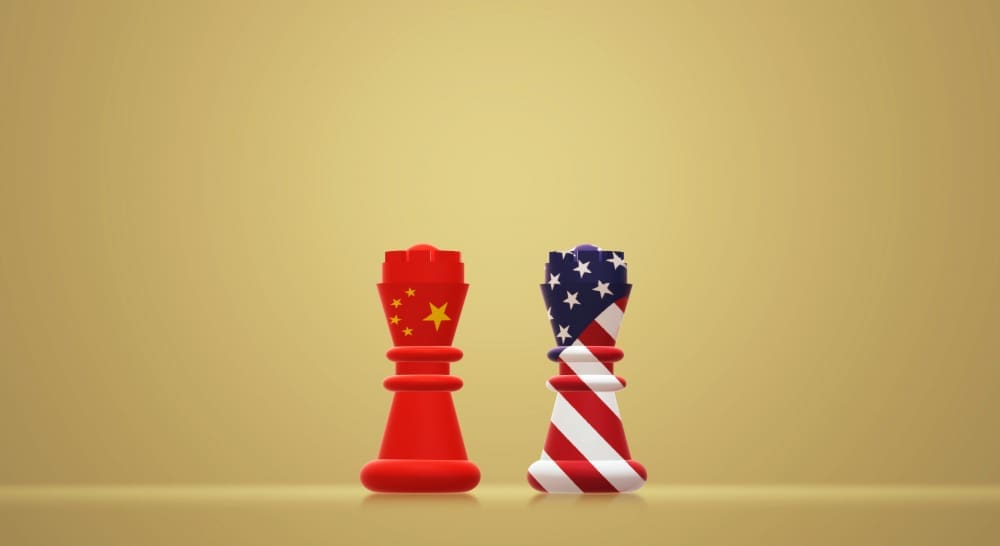 Two stylized chess rooks, one red with a Chinese flag design and the other striped with an American flag design, stand facing each other on a golden surface, symbolizing a geopolitical standoff.