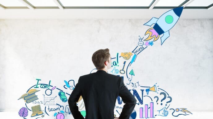 A businessman seen from behind, looking at a wall covered with colorful doodles of a launching rocket, ideas, and business concepts, symbolizing goal setting.