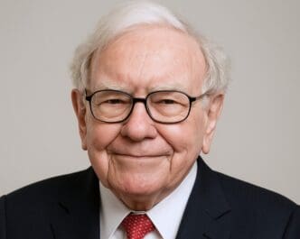 Close-up headshot of Warren Buffett, smiling and wearing glasses, against a light background.
