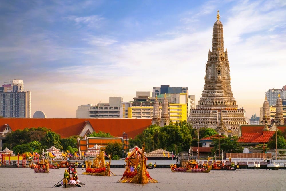 A view of Wat Arun (Temple of Dawn) in Bangkok, Thailand, overlooking the Chao Phraya River with ceremonial boats.