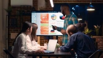 An African American employee presents an analytics report with statistics on a digital screen during a business meeting.