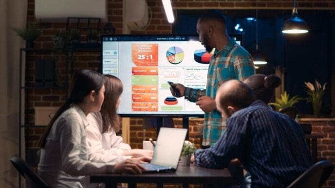An African American employee presents an analytics report with statistics on a digital screen during a business meeting.