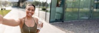 African American woman smiles while holding a cellphone and a bottle of water, recording a video for her blog.