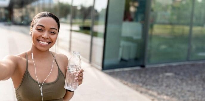 African American woman smiles while holding a cellphone and a bottle of water, recording a video for her blog.