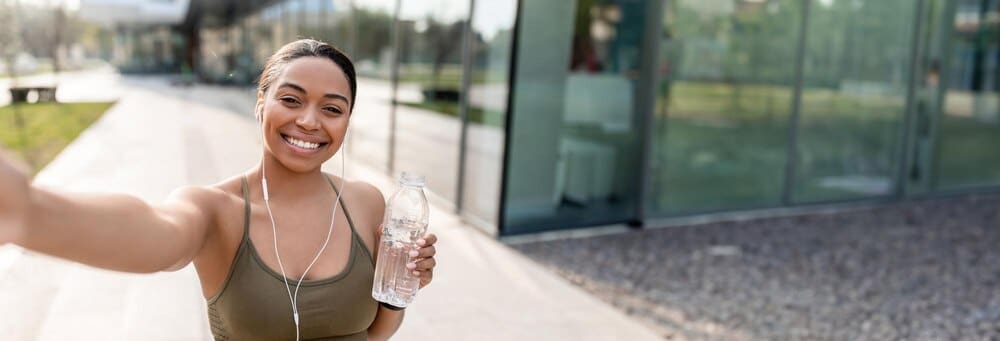 African American woman smiles while holding a cellphone and a bottle of water, recording a video for her blog.