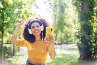 A Black girl with an afro dances joyfully in a park, wearing headphones and listening to music.