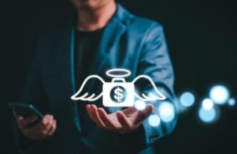 A businessman holds a money bag icon with wings, representing an angel investor concept.