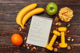 A still life shows an apple, an orange, and two dumbbells, symbolizing a healthy lifestyle.