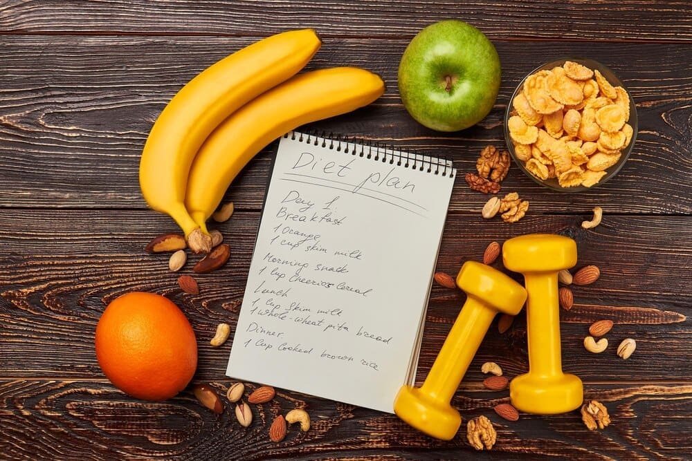 A still life shows an apple, an orange, and two dumbbells, symbolizing a healthy lifestyle.