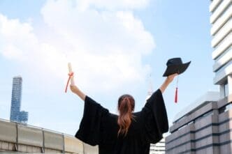 Two Asian women in graduation gowns hold their diplomas and smile.