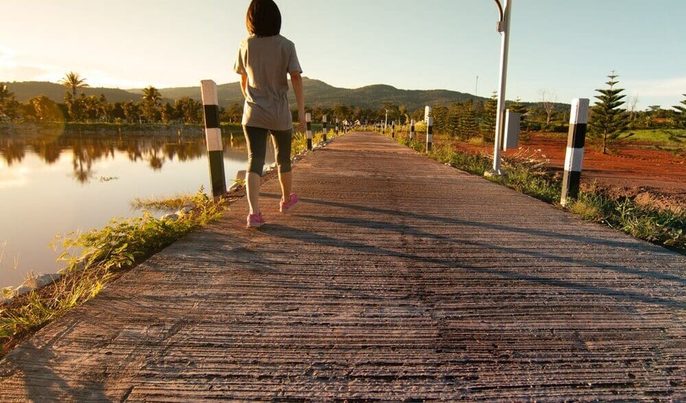 A young Asian woman in fitness attire walks along a path in a tropical park after running.