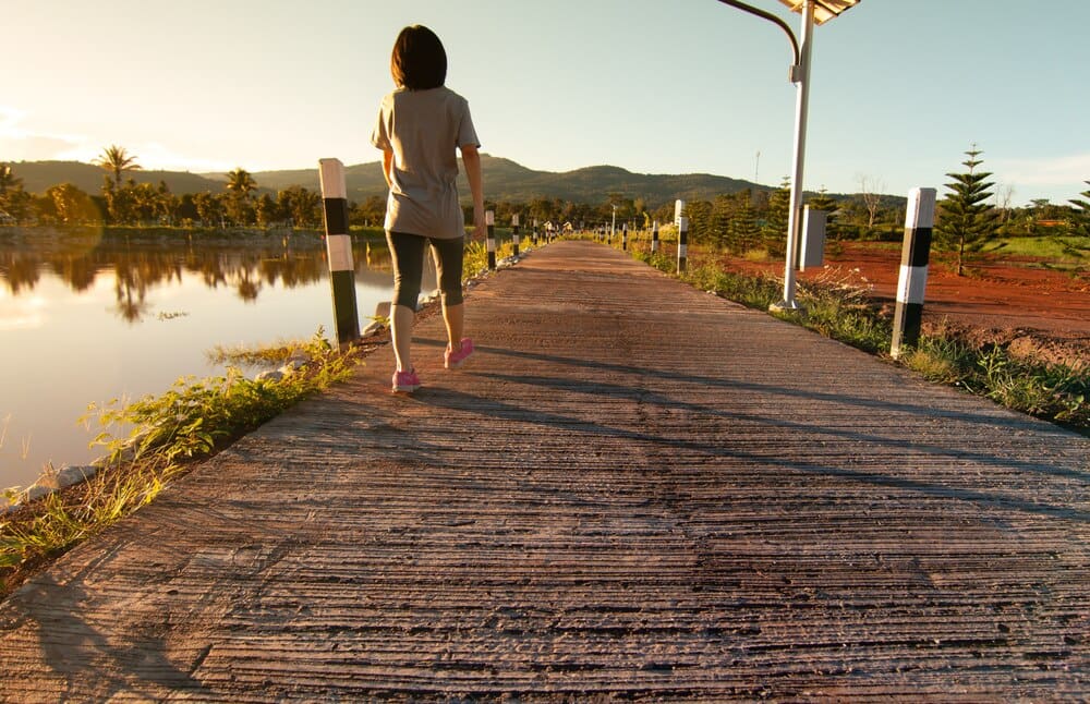 A young Asian woman in fitness attire walks along a path in a tropical park after running.