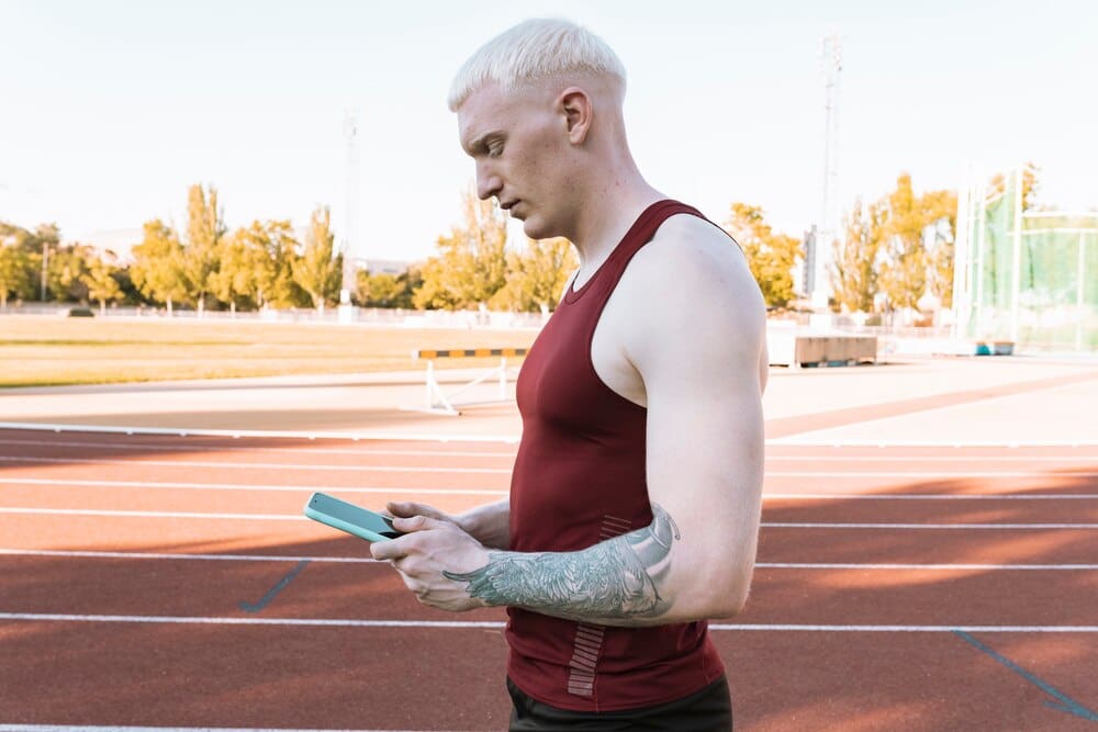 A male athlete on a running track looks down at his smartphone.
