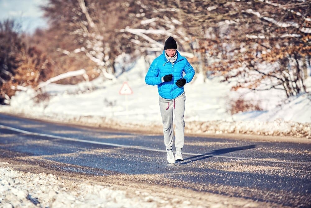 An athletic man jogs and trains outdoors in a park with snow on a cold day.