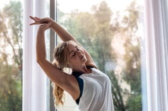 An attractive woman practices pilates yoga near a window, promoting a healthy lifestyle.