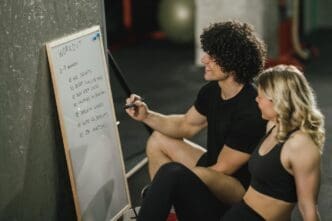 An attractive woman and her personal trainer discuss an exercise plan in a gym setting.