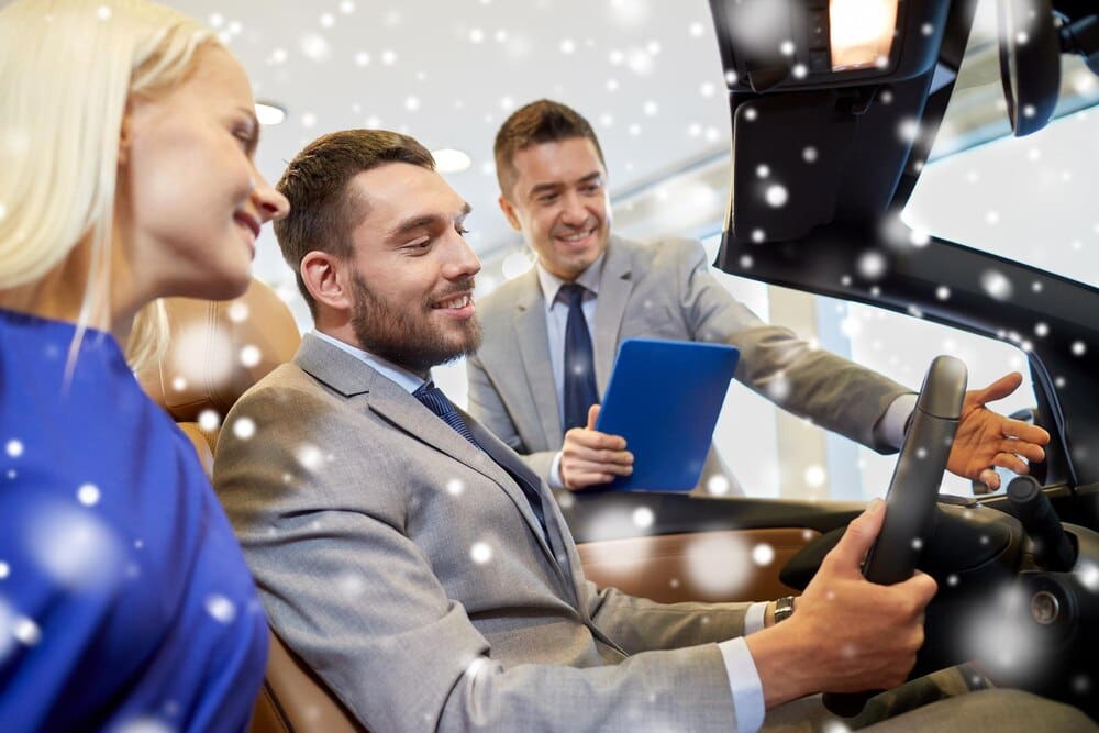 A happy couple and a car dealer stand together in a car showroom with a snowy effect overlay.