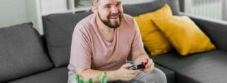 A young man smiles while playing video games on a sofa, with copy space suggesting themes of gaming addiction.