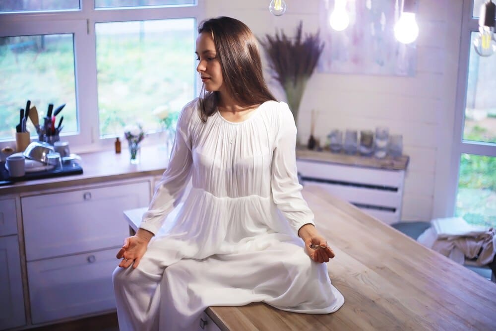 A young woman in athletic wear sits in the lotus position, meditating indoors.
