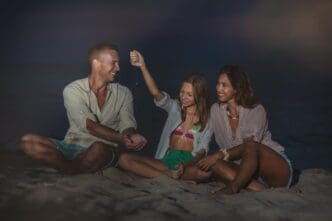 A smiling family enjoys an evening on a sandy beach, playing together.