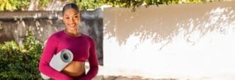 A young Black woman in pink workout clothes smiles while exercising outdoors in a garden.