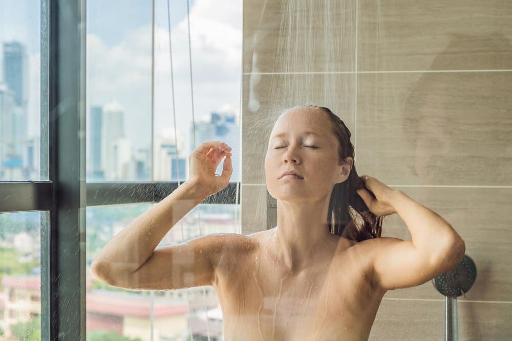 A woman showers behind glass, with water drops obscuring the view of a city skyline.