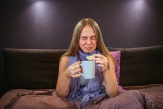 A young woman grimaces while holding a lemon and a cup of tea.