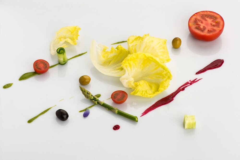 Sliced tomatoes and asparagus are artistically arranged on a white surface.
