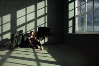 A black angel with outstretched wings looks out a window, representing the concept of freedom.