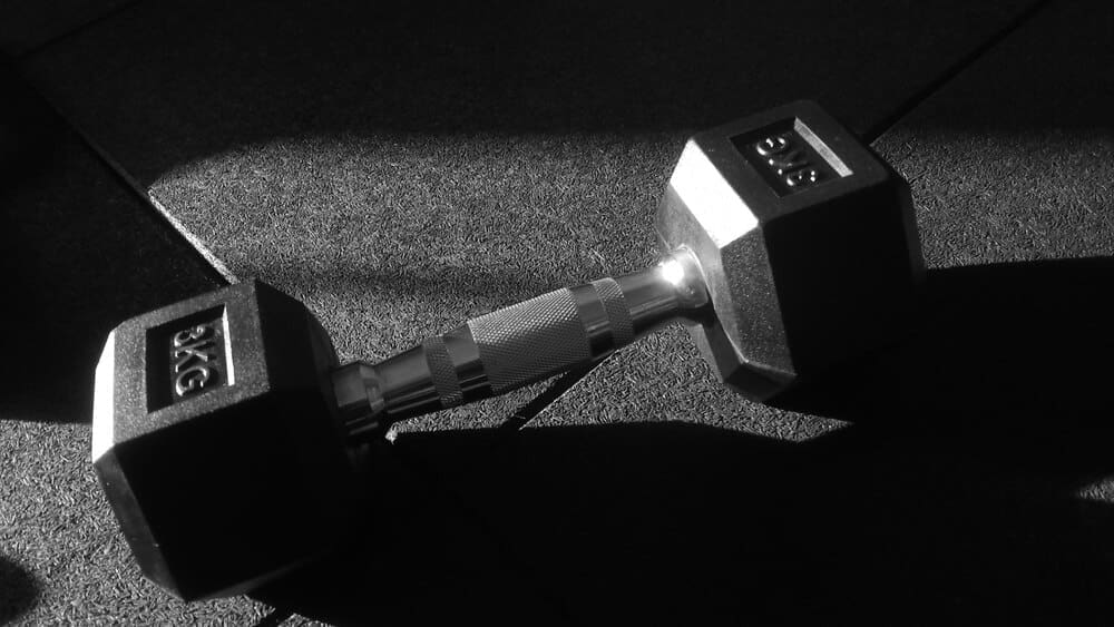 Black and white photo shows a 3 kg dumbbell resting on the floor.