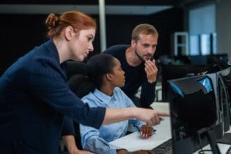 Two business colleagues, a man and a woman, collaborate in cybersecurity at a desk in a modern office setting.