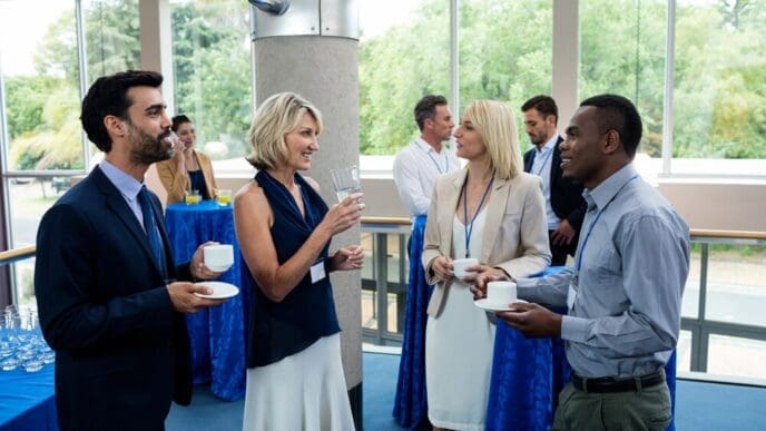 Business executives in suits and ties converse and gesture while sitting around a table with coffee cups.