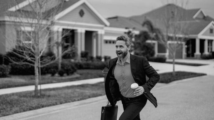 A businessman in a suit runs down a street in a residential neighborhood.