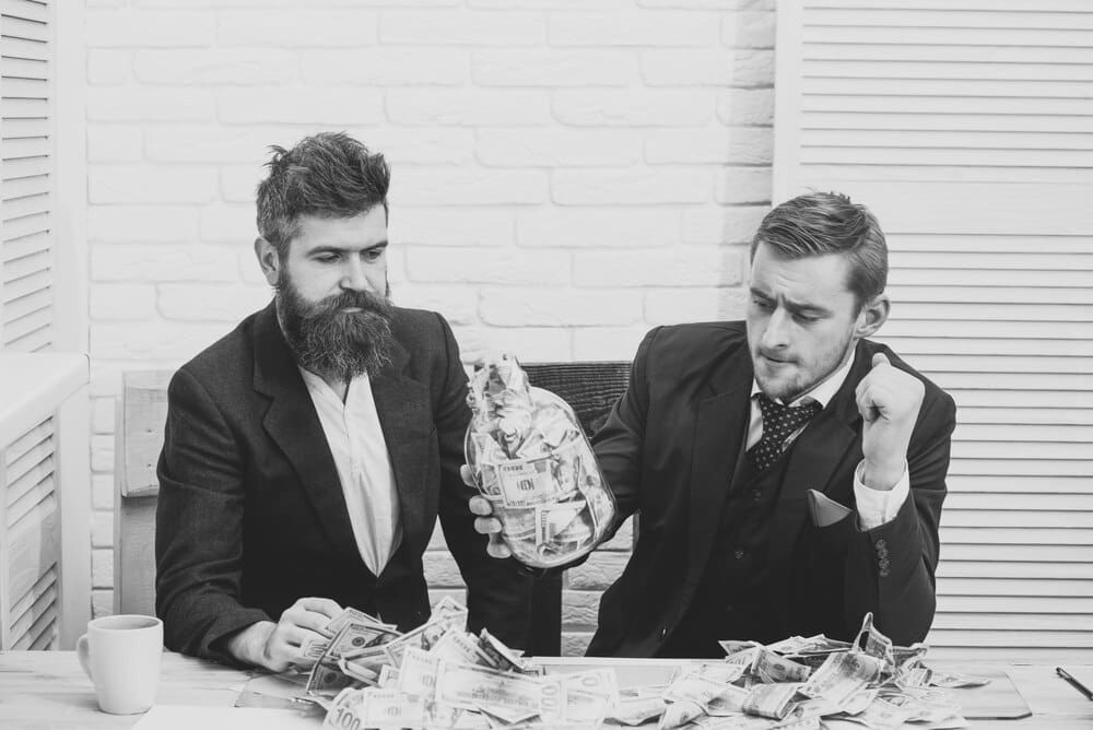 Business partners looking thoughtful at a meeting with a jar of cash in an office.